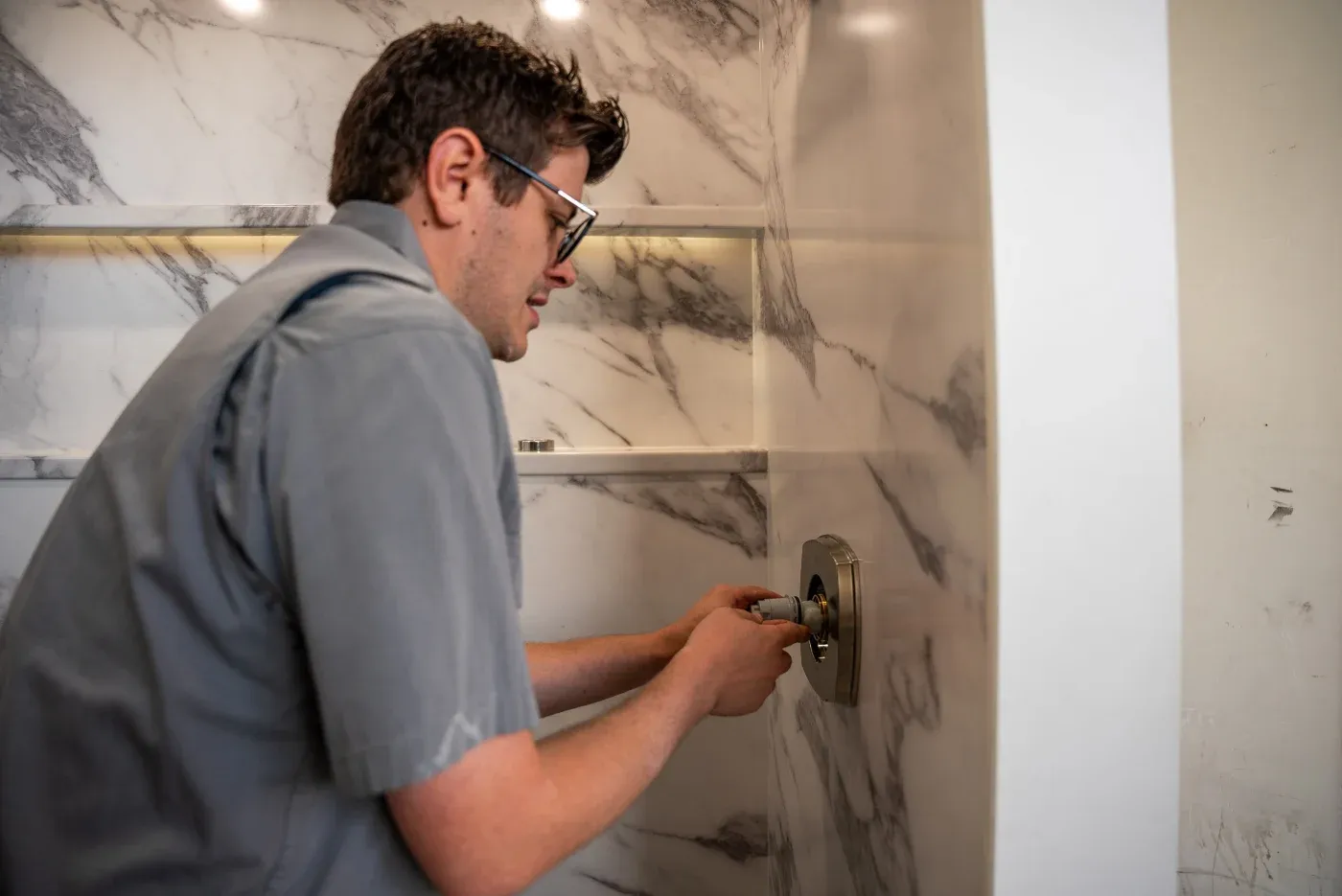 A certified factory-trained walk-in shower installer with Twist & Spout in Northwest AR working on hardware in a newly-installed walk-in shower.