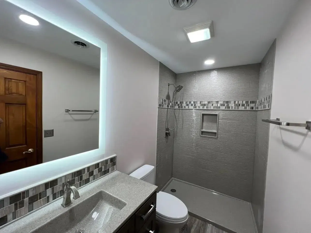 A newly remodeled bathroom with a luxurious walk-in shower with no entry door, custom tile work, and new hardware, including a hand-held showerhead.