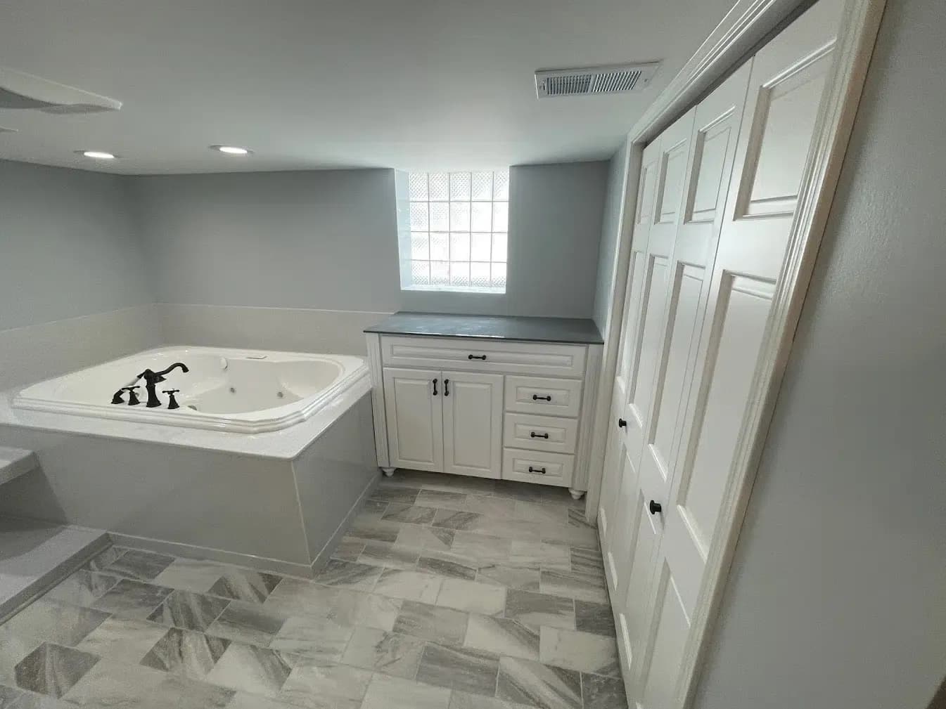 A light gray bathroom with white cabinets and a large white jacuzzi soaking tub in an alcove on the left.