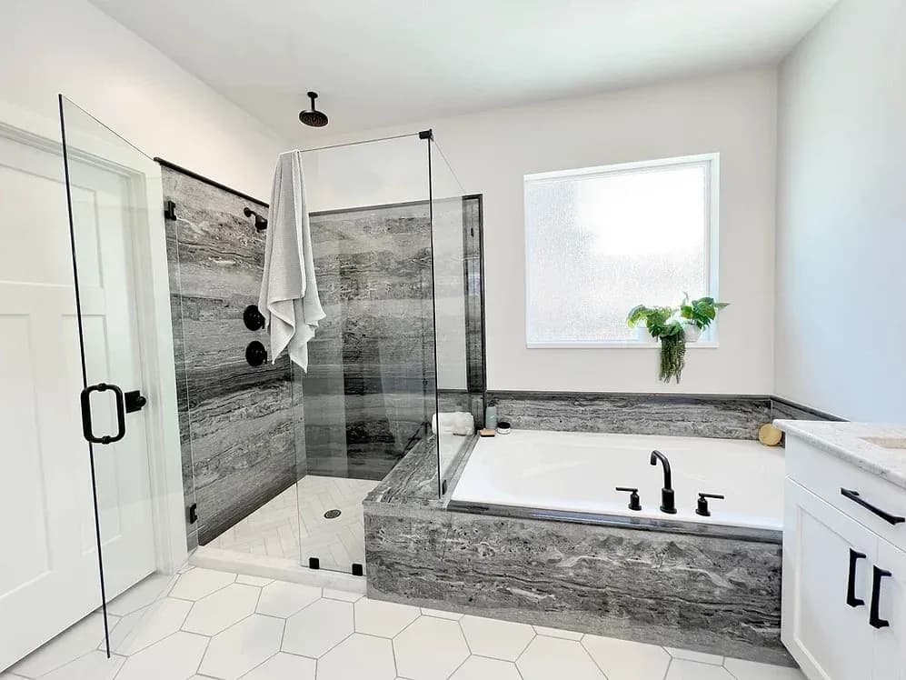 A newly remodeled residential bathroom that’s black and white, with a new walk-in shower with glass walls and door and a luxurious new bathtub.